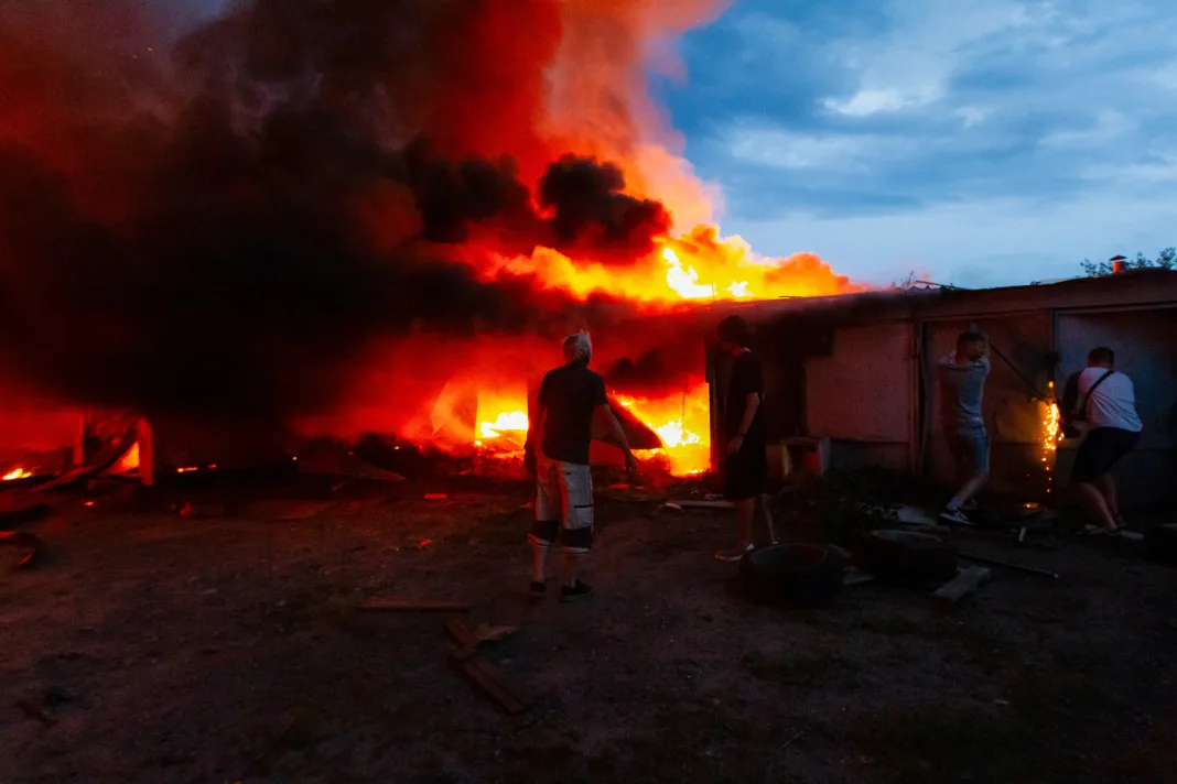 Men stand beside garages engulfed in flames following a massive combined Russian attack, Kyiv, Ukraine, on July 6, 2026. Russian forces launched a large-scale attack on the capital using ballistic and cruise missiles as well as attack drones, causing destruction to apartment buildings and civilian infrastructure across several districts of the city. The Podilskyi district suffered the most severe damage. At least 11 people were killed and 46 others were injured (Photo by Kyrylo Chubotin/Ukrinform/ABACAPRESS.COM